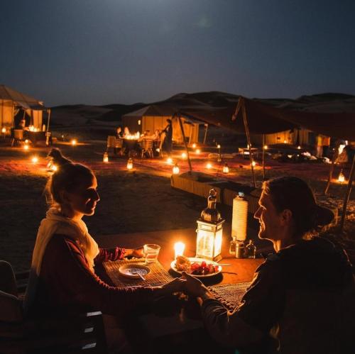 a man and woman sitting at a table at night at Merzouga Hamza Luxury Camp in Merzouga