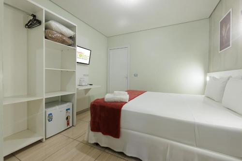 a white bedroom with a bed and shelves at Hotel e Pousada Caroline in Foz do Iguaçu