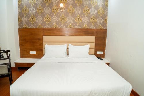 a bedroom with a white bed with a wooden headboard at Grand Hridey 1 minute from Railway Station in Amritsar