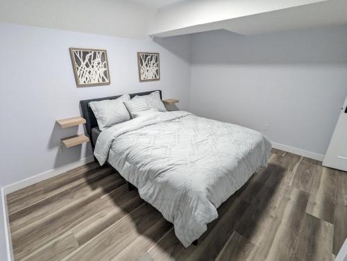 a white bedroom with a bed and a wooden floor at Chic 2BR Suite with Kitchen, Laundry, Near Elk Island & West Edmonton Mall in Edmonton