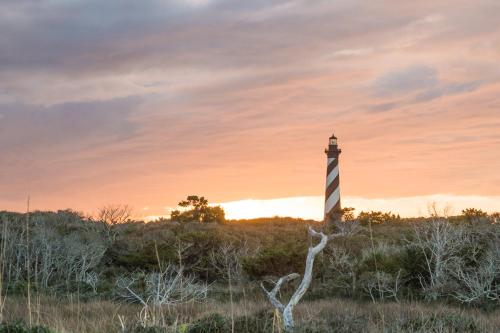 a lighthouse in a field with the sunset in the background at Watermen's Cabana 1B - 2-Bed, 1-Bath Apartment - Walk To BEACH Access & PET Friendly! in Waves