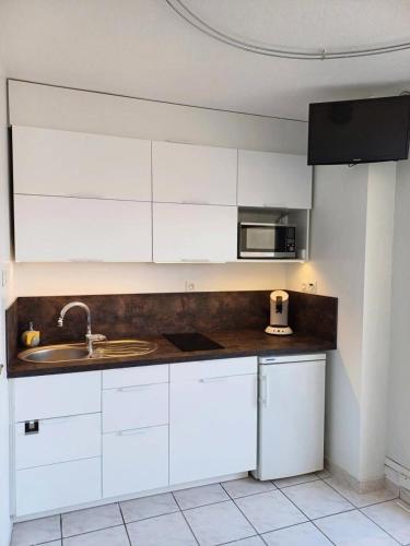 une cuisine avec des armoires blanches, un évier et un micro-ondes dans l'établissement Résidence Héliopolis Bâtiment E - studio 2 Pers. Héliopolis Bât. E MAE-4474, au Cap d'Agde