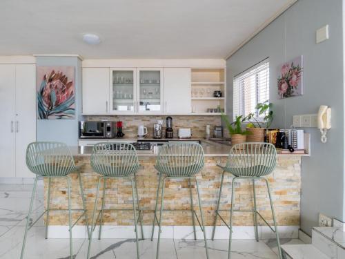 a kitchen with three bar chairs and a counter at Lagoon Shoreline Penthouse in Cape Town