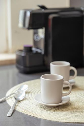 two coffee cups sitting on a plate next to a coffee maker at 2-bedroom gem Central Odivelas in Odivelas