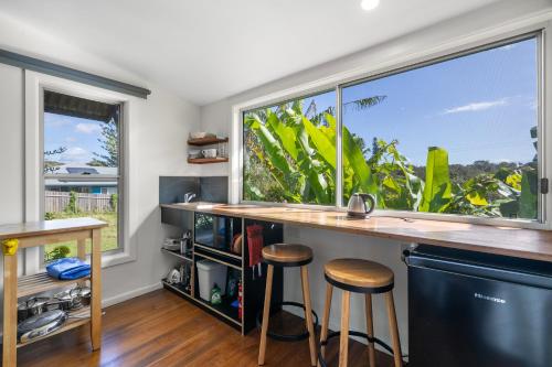 a kitchen with two windows and a counter with stools at Korogoro Beach House in Hat Head