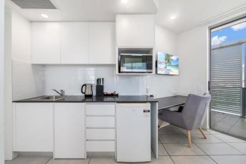 a kitchen with white cabinets and a sink and a desk at North Shore Oceanside Kawana in Kawana Waters