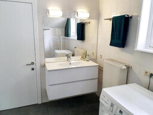 a white bathroom with a sink and a mirror at Les Bruyeres in De Haan