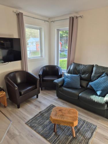 a living room with a black leather couch and two chairs at Séjour Flèche du fjord vue Saguenay Mont Valin in Saint-Fulgence
