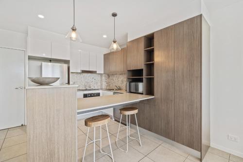 a kitchen with wooden cabinets and bar stools at North Shore Oceanside Kawana in Kawana Waters