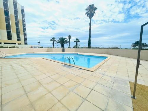 une piscine avec un palmier en arrière-plan dans l'établissement Superbe appartement avec piscine et parking sécurisé - FR-1-748-33, à Canet