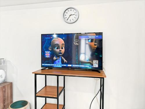 a television on a stand with a clock on the wall at Cozy 3BR M-Town apt Serpong with Pool by 2ndHome in Pumpangsineng