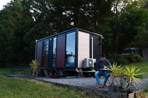 a man sitting in front of a tiny house at Little Enniskillen by Tiny Away in Kurrajong