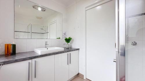 Un baño blanco con lavabo y espejo. en Lucerne Escape by GoodLive, en Frankston