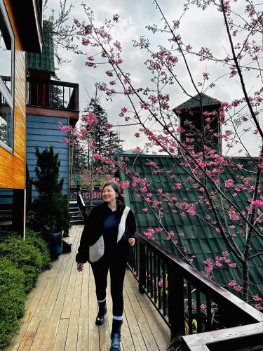 a woman walking down a wooden walkway with pink flowers at Sapa Pine Hill Eco Lodge in Sa Pa