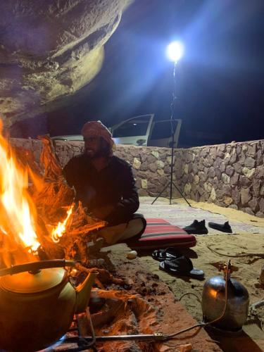 a man sitting next to a camp fire at Wadi Rum Starlit in Wadi Rum