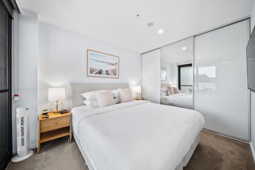 a white bedroom with a large bed and a glass wall at Stylish 2-Bed Apartment in Canberra CBD in Canberra