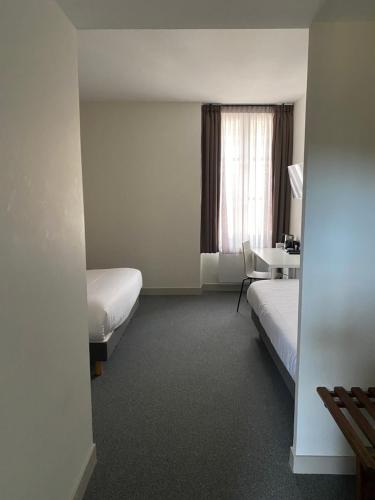 a room with two beds and a desk and a window at Le Relais du Château in Saint-Fargeau