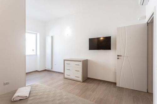 a white bedroom with a dresser and a tv on a wall at ApartHotel Angelo - Salento Reservation in Racale