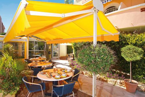 a yellow umbrella on a patio with tables and chairs at Logis Hotel l'Esterella in Agay - Saint Raphael