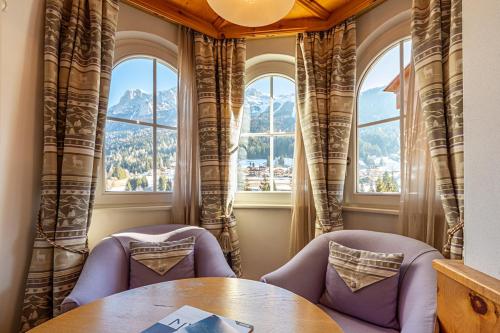 a room with two chairs and a table and two windows at Hotel Des Alpes in Soraga