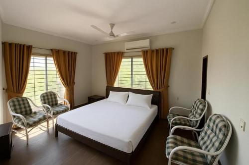 a bedroom with a white bed and two chairs at Farm House Angoori Hill Near Bahria Golf City in Rawalpindi
