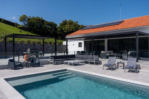 a patio with a pool and chairs and a house at Casa Pura Vida - Heated Pool and Sea View in Ponta Delgada