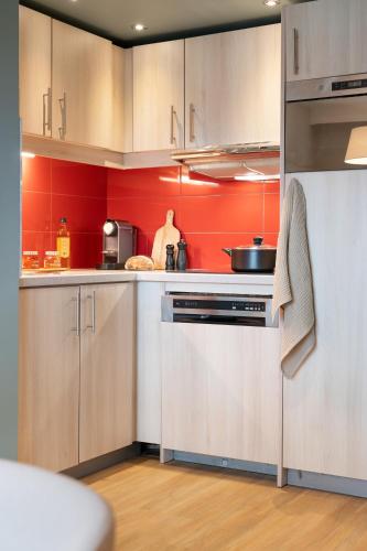 a kitchen with red walls and wooden cabinets at Résidence Pierre & Vacances Premium Haguna in Biarritz