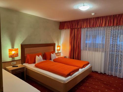 sypialnia z łóżkiem z pomarańczową pościelą i oknem w obiekcie Hotel Garni Wolfgang w Saalbach Hinterglemm