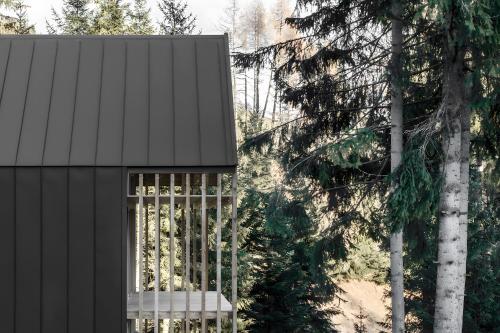 a black house with a bench next to some trees at Waldchalets Obomilla in Maranza