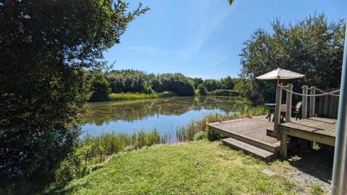 a wooden deck with an umbrella next to a river at Lynstone Lakes in Bude
