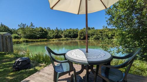 a table with an umbrella and chairs next to a river at Lynstone Lakes in Bude