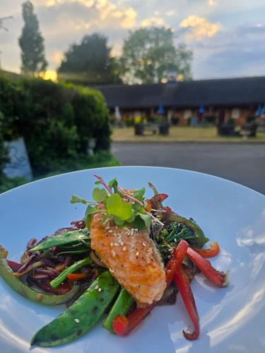 a white plate of food with fish and vegetables at The Royal Arms Hotel in Sutton Cheney