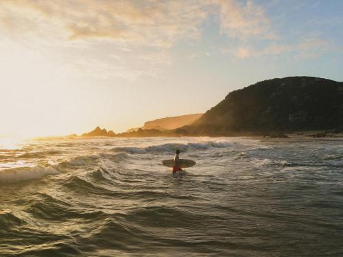 a person standing in the ocean with a surfboard at Buccara Noetzie - Pezula Castle in Knysna