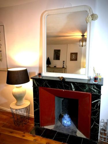 un miroir au-dessus d'une cheminée avec une lampe et une table dans l'établissement Les Remparts - Centre Ville - Charme & Vue Montagnes, à Barcelonnette
