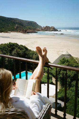 a woman laying in a chair reading a book next to the beach at Buccara Noetzie - Pezula Castle in Knysna