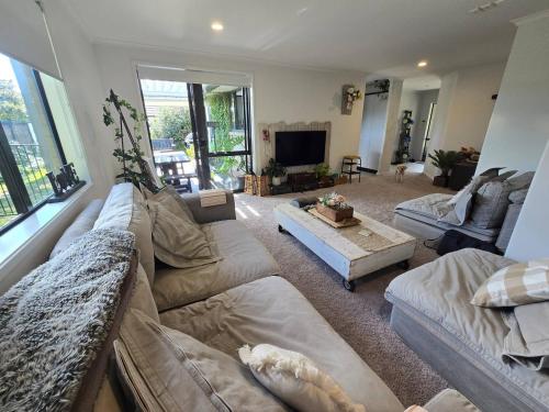 a living room with a large couch and a tv at Bethlehem Home, plus Self Contained Apartment in Tauranga