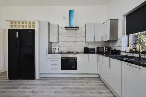 a kitchen with white cabinets and a black refrigerator at Hayy Luxury Retreat At The Lodge in Bradford