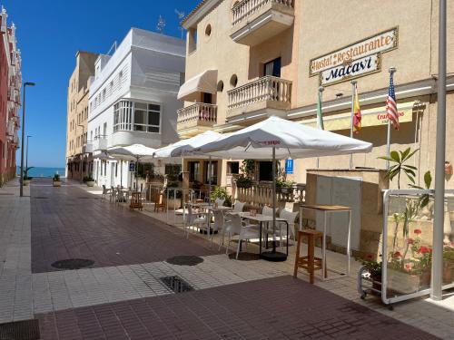 an outdoor cafe with tables and umbrellas on a street at Hotel Macavi Playa in Rota