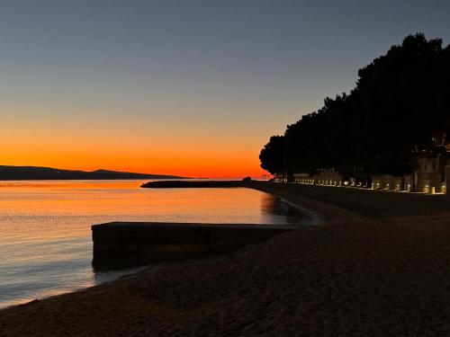 a sunset on a beach with trees and the water at Guesthouse on the beach in Baška Voda