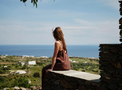 a woman sitting on a stone wall looking at the view at Stamna Sifnos a member of Design Hotels in Sifnos