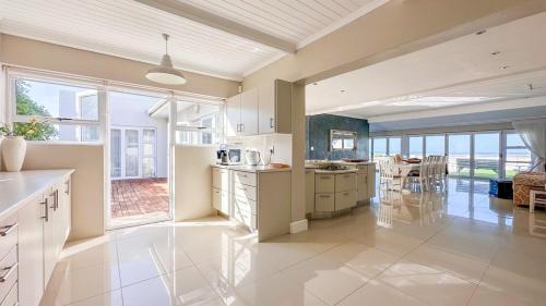 a large kitchen with white cabinets and a large window at Die Lig-Huis Struisbaai in Struisbaai