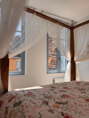 a bedroom with a bed with a canopy and two windows at La Cour des Murmures - Logis central d'exception - in Troyes