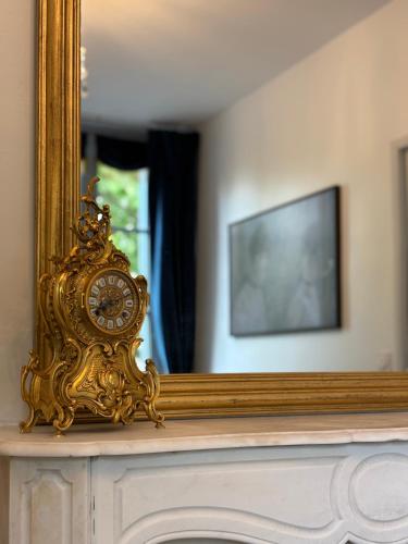 une horloge en or posée sur une cheminée devant un miroir dans l'établissement La Cour des Murmures - Logis central d'exception -, à Troyes