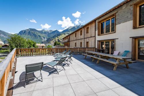 a patio with tables and chairs and mountains at Renovated apartment with terrace for 14 people in Saint-Jean-de-Maurienne