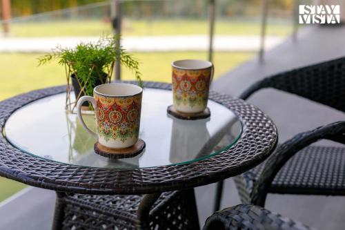 two coffee mugs sitting on a glass table at StayVista's The Tavern At Canary Farms - Mountain-View Luxury Mansion with Infinity Pool & Games Zone in Lonavala