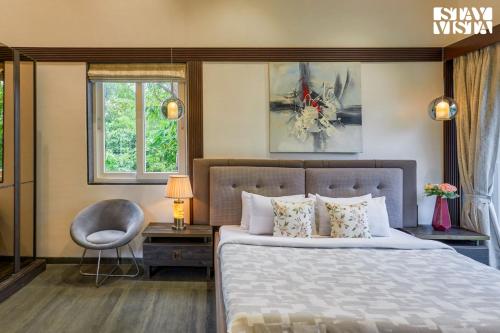 a bedroom with a bed and a chair and windows at StayVista's The Tavern At Canary Farms - Mountain-View Luxury Mansion with Infinity Pool & Games Zone in Lonavala