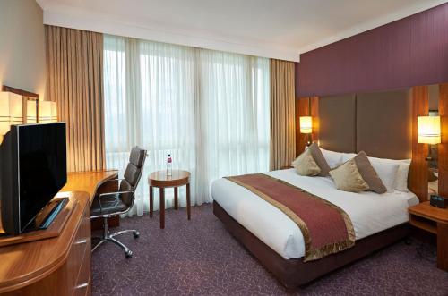 a hotel room with a bed and a desk and a television at Crowne Plaza London Ealing by IHG in London