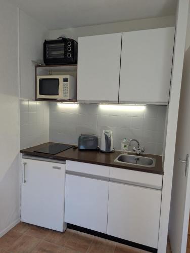 a kitchen with white cabinets and a sink and a microwave at Studio cosy Anemone in Luchon