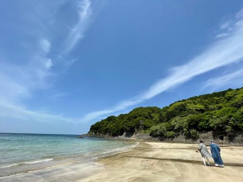 two people walking on a beach near the ocean at ぽつんとオーシャンビューでバーベキューも出来る1日1組貸切宿カゴヤブハウス in Otsuki