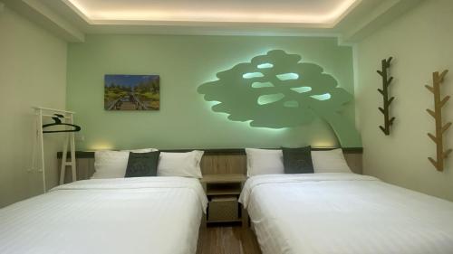 two beds in a room with a tree on the wall at 台東漫活電梯民宿-可包棟 in Taitung City